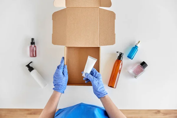 Mãos em luvas embalagem caixa de pacote com cosméticos — Fotografia de Stock