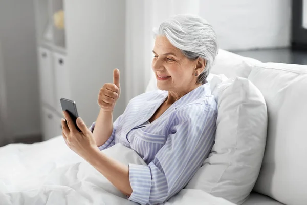 Пожилая женщина с телефоном с видеозвонком в постели — стоковое фото