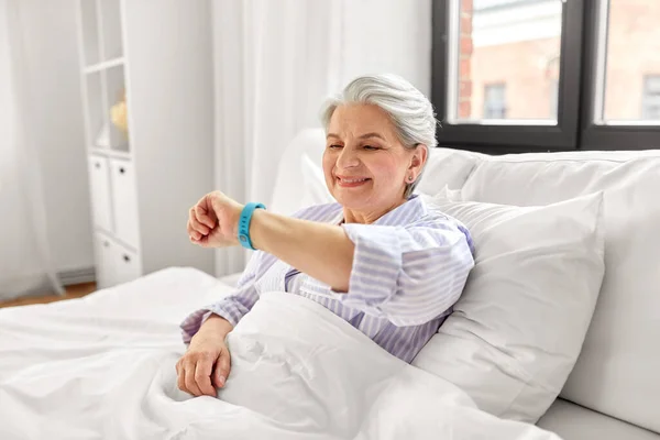 Wanita tua bahagia dengan pelacak kesehatan duduk di tempat tidur — Stok Foto