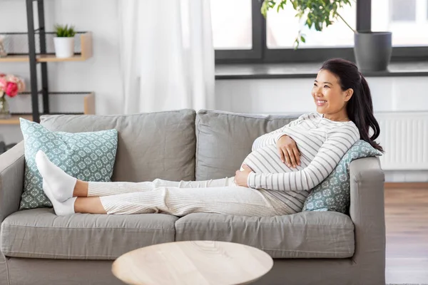 Šťastný těhotná asijské žena sedí na pohovce doma — Stock fotografie