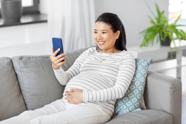 Mujer embarazada feliz con teléfono inteligente en casa — Foto de Stock