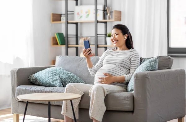 Schwangere mit Telefon und Kopfhörer zu Hause — Stockfoto