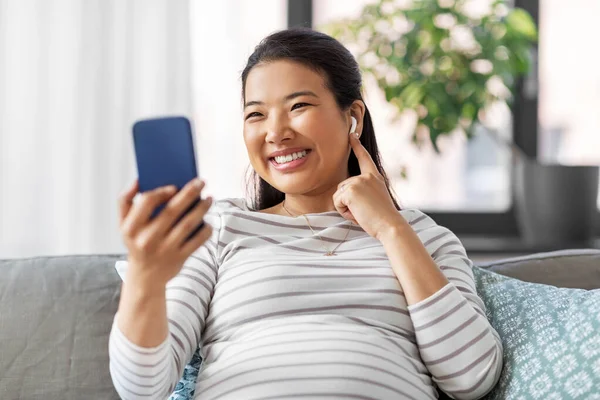 Femme enceinte avec téléphone et écouteurs à la maison — Photo