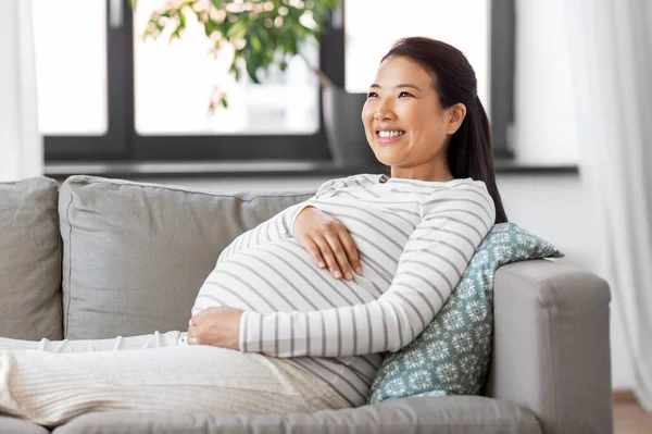 Feliz grávida asiática mulher sentada no sofá em casa — Fotografia de Stock