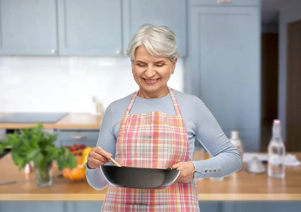 Donna anziana sorridente in grembiule con padella — Foto Stock