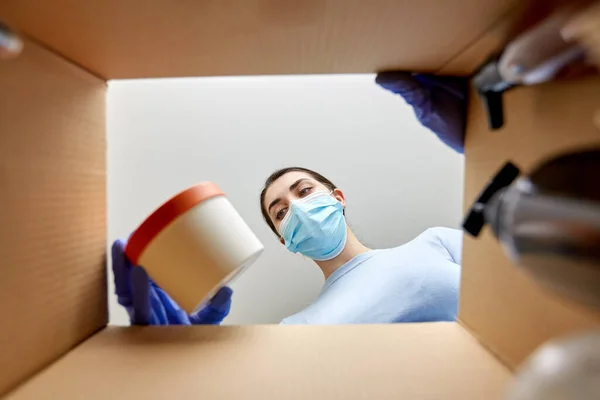 Kvinna i mask packa upp paket låda med kosmetika — Stockfoto