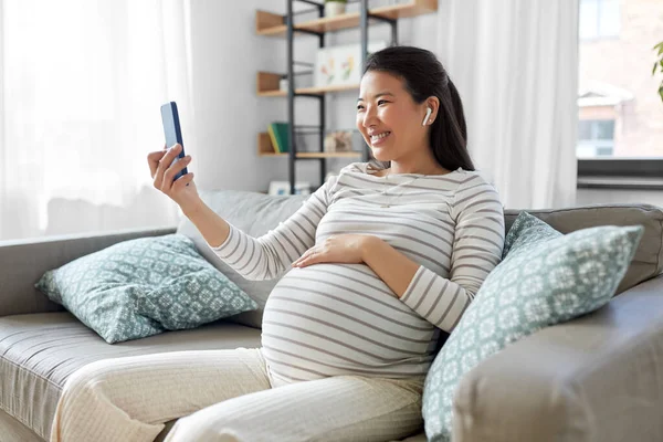 Femme enceinte avec téléphone et écouteurs à la maison — Photo