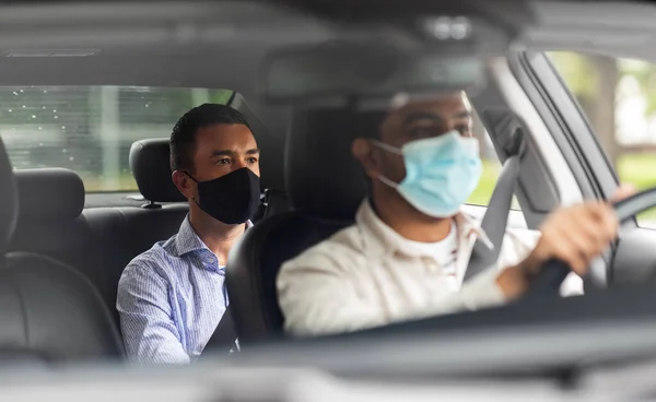Водитель в маске за рулем автомобиля с пассажиром — стоковое фото