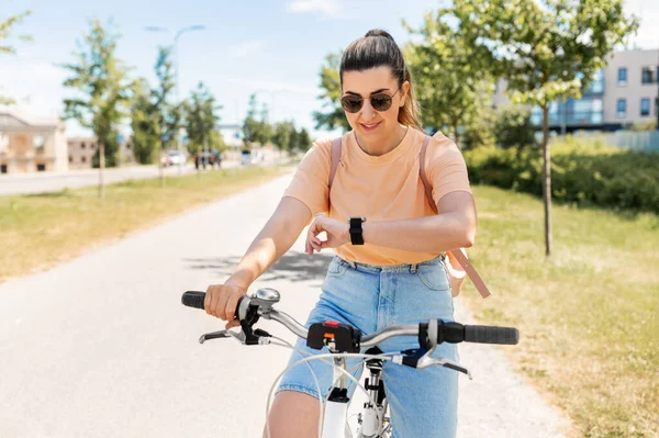 Vrouw met slim horloge paardrijden fiets in de stad — Stockfoto