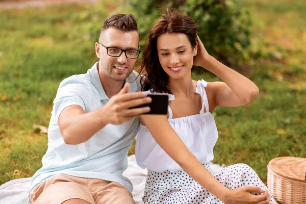 Feliz pareja tomando selfie en el picnic en el parque —  Fotos de Stock