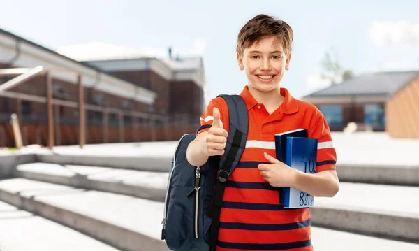 Studentský chlapec s taškou a knihami ukazujícími palce nahoru — Stock fotografie