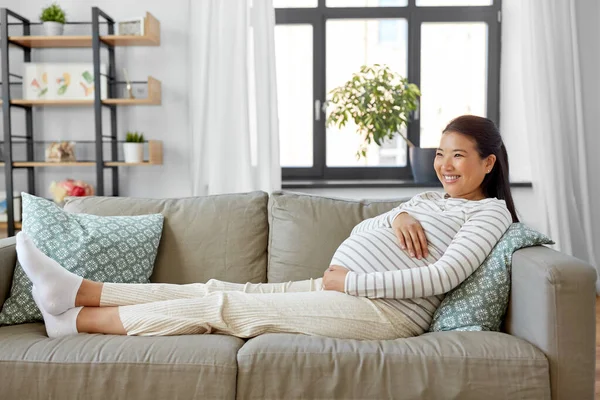 Glad gravid asiatisk kvinna sitter på soffan hemma — Stockfoto