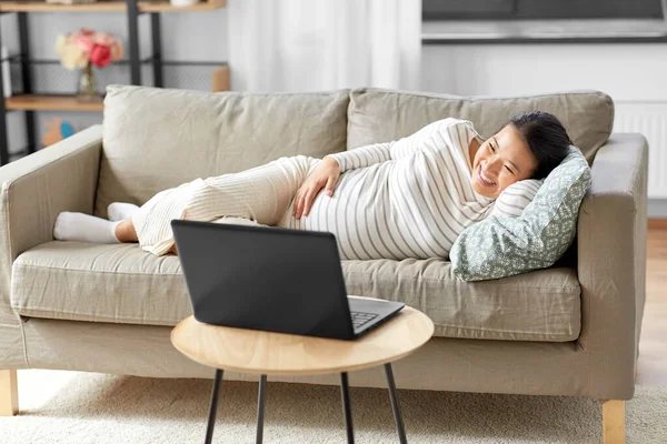 Щаслива вагітна азіатка з ноутбуком вдома — стокове фото