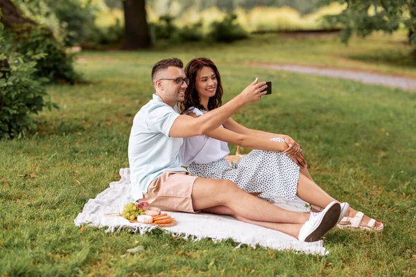 Feliz pareja tomando selfie en el picnic en el parque —  Fotos de Stock