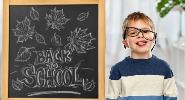 Liten student pojke i glasögon som visar tungan — Stockfoto