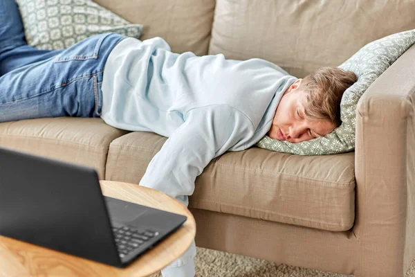Hombre aburrido con el ordenador portátil tumbado en el sofá en casa —  Fotos de Stock