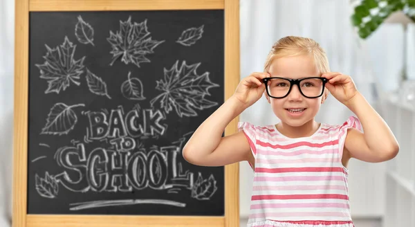 Little student girl in glasses over chalkboard — Stock Photo, Image