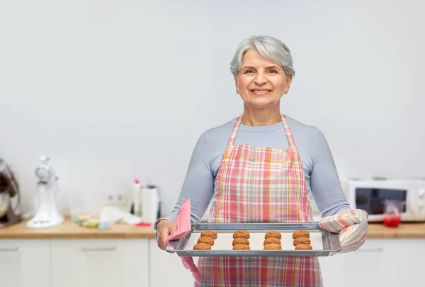 Mujer mayor en delantal con galletas en bandeja para hornear — Foto de Stock