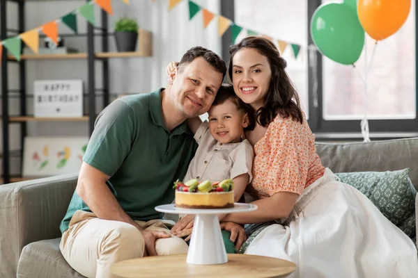 Família feliz com bolo de aniversário abraçando em casa — Fotografia de Stock