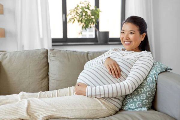 Feliz grávida asiática mulher sentada no sofá em casa — Fotografia de Stock
