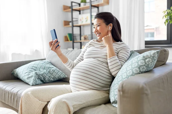 Mulher grávida com telefone e fones de ouvido em casa — Fotografia de Stock