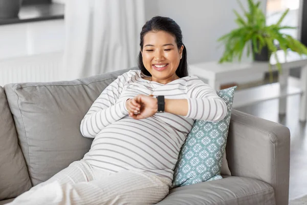 Счастливая беременная женщина с умными часами дома — стоковое фото