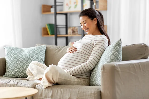 Heureux enceinte asiatique femme assis sur canapé à la maison — Photo