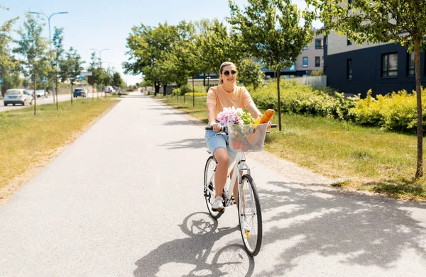 Vrouw met eten en bloemen in fietsmand — Stockfoto