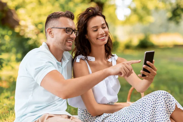 在公园野餐的时候带着智能手机的快乐夫妇 — 图库照片