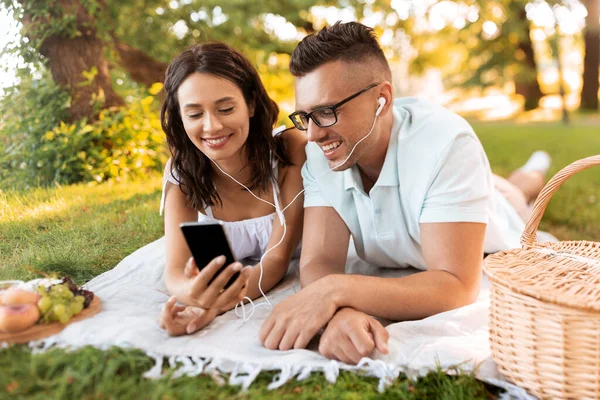 Pareja con auriculares y smartphone en el picnic —  Fotos de Stock