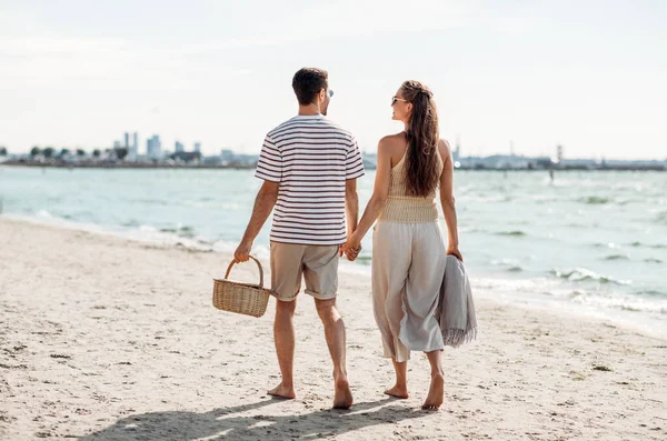 Szczęśliwa para z koszykiem piknikowym spacerująca po plaży — Zdjęcie stockowe