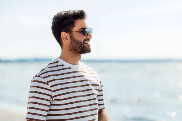 Glimlachende jonge man in een zonnebril op het zomerstrand — Stockfoto