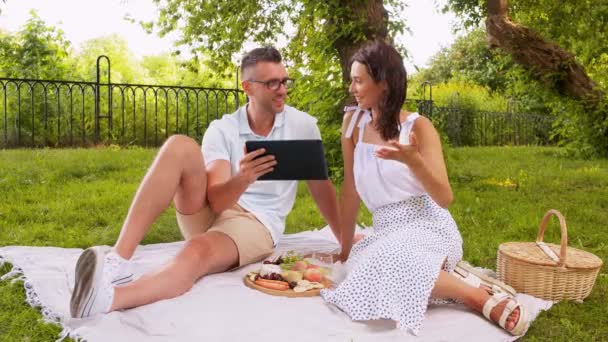 Lyckligt par med surfplatta på picknick i parken — Stockvideo