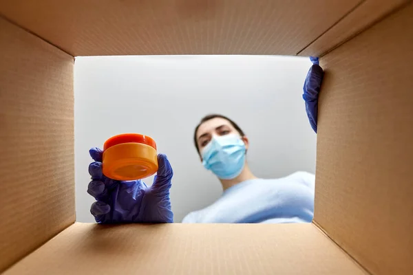 Woman in mask unpacking parcel box with cosmetics — Stock Photo, Image