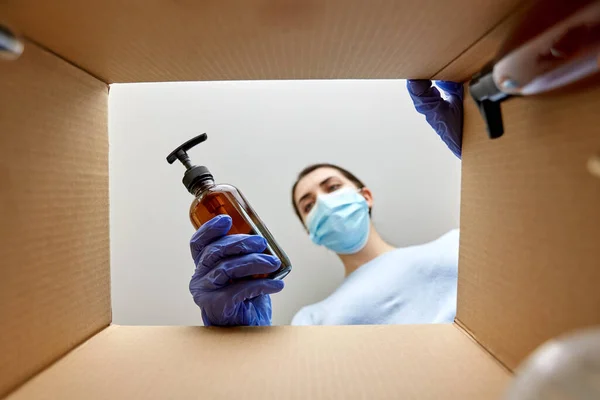 Woman in mask unpacking parcel box with cosmetics — Stock Photo, Image