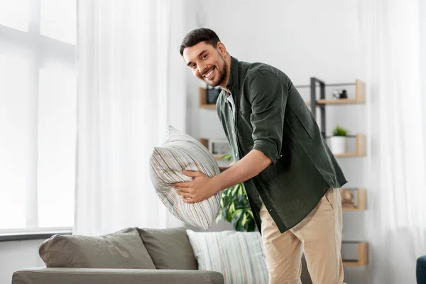 Щасливий усміхнений чоловік влаштовує диванні подушки вдома — стокове фото