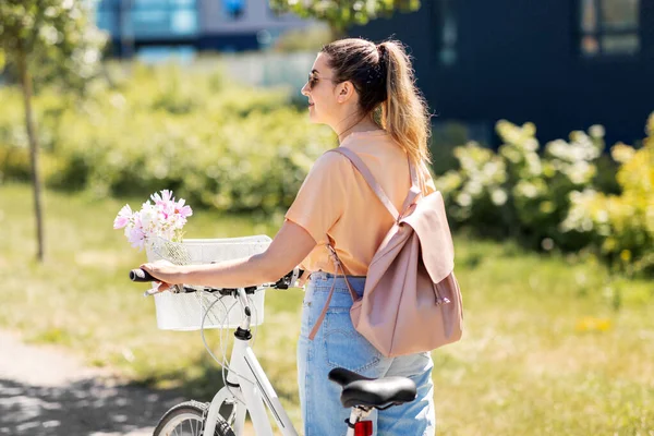 Donna con fiori nel cestino della bicicletta in città — Foto Stock