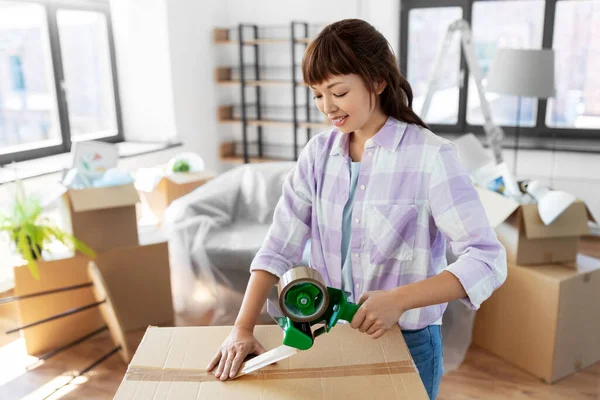 Frau mit Klebeband-Verpackungsbox im neuen Zuhause Stockbild