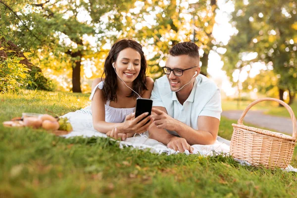 Koppel met oortjes en smartphone bij picknick — Stockfoto