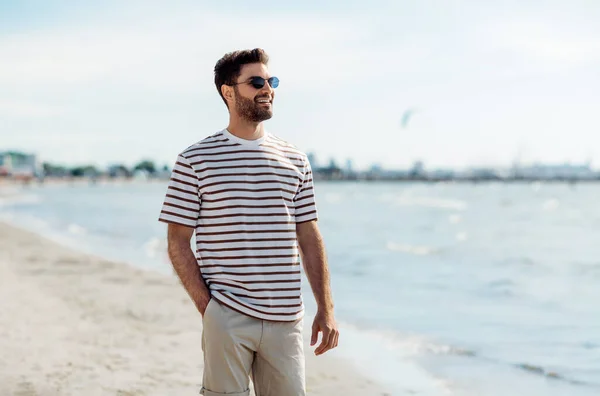 Улыбающийся молодой человек в солнечных очках на летнем пляже — стоковое фото
