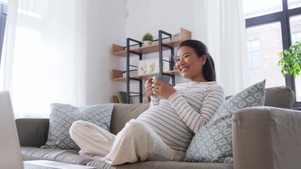 Счастливая беременная азиатка с ноутбуком дома — стоковое видео