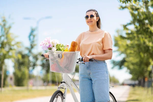 Femme avec de la nourriture et des fleurs dans le panier à vélo — Photo