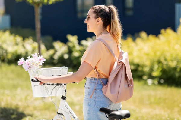 Donna con fiori nel cestino della bicicletta in città — Foto Stock