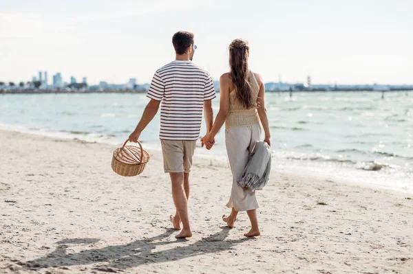 Szczęśliwa para z koszykiem piknikowym spacerująca po plaży — Zdjęcie stockowe