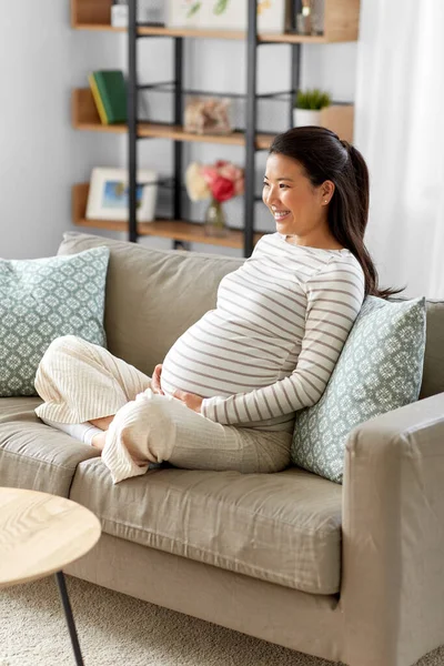 Glad gravid asiatisk kvinna sitter på soffan hemma — Stockfoto