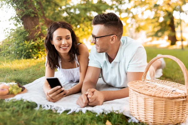 Pareja feliz con teléfono inteligente en el picnic en el parque — Foto de Stock