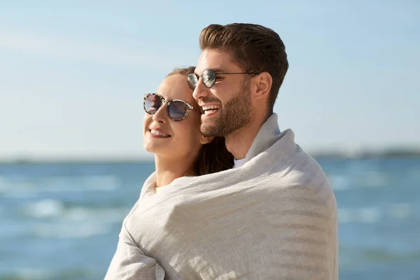 Feliz pareja cubierta con manta abrazos en la playa —  Fotos de Stock