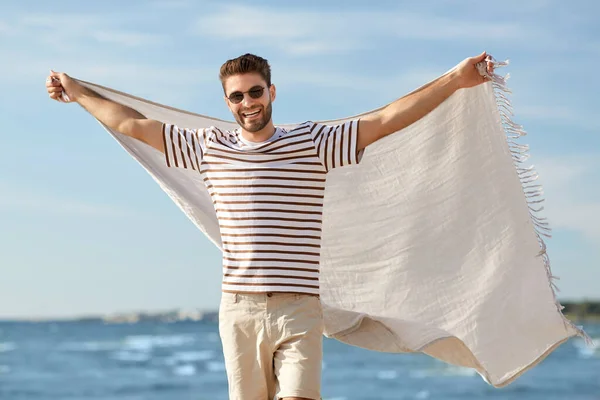 Uomo sorridente in occhiali da sole con coperta sulla spiaggia — Foto Stock