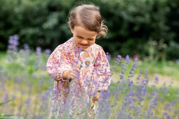 庭の花を見て拡大鏡を持つ女の子 — ストック写真