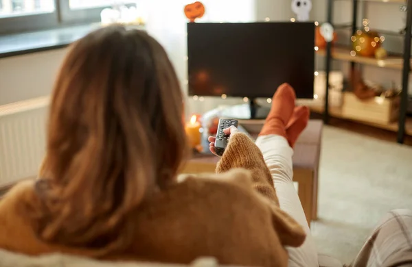 Молода жінка дивиться телевізор вдома на Хеллоуїн — стокове фото
